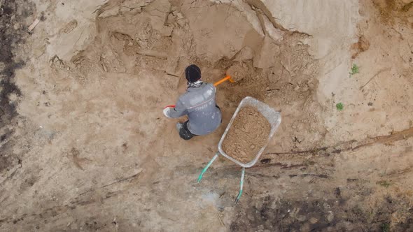 An Aerial View. A Worker in Special Clothes Digs a Sand Heap. A Light Shovel in Action.