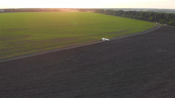 A Small Airplane Takes Off From a Field.at Sunrise