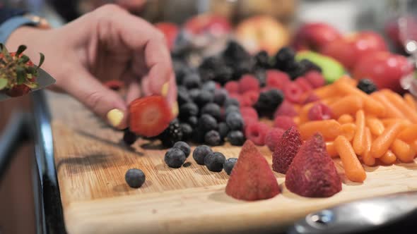 Close up of woman slicing stems off fresh strawberries with kitchen knife.