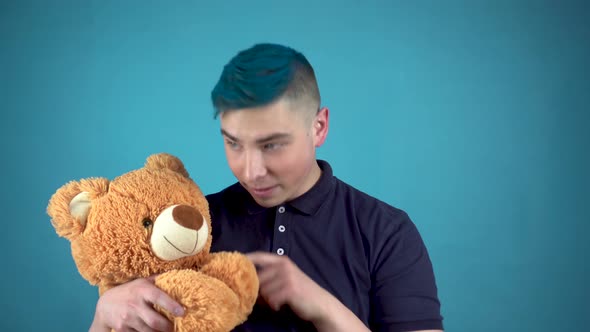 A Young Man with Blue Hair Is Holding a Teddy Bear. Alternative Man Waves His Hand and Looks at the