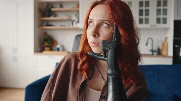 Adult Redhaired Girl with a Modern Hightech Prosthesis Instead of an Amputated Arm Sits in Thought