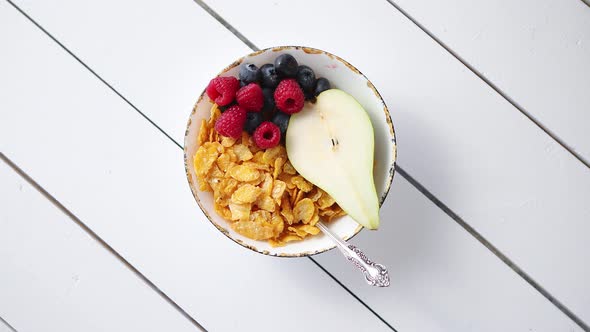 Golden Cornflakes with Fresh Fruits of Raspberries, Blueberries and Pear in Ceramic Bowl