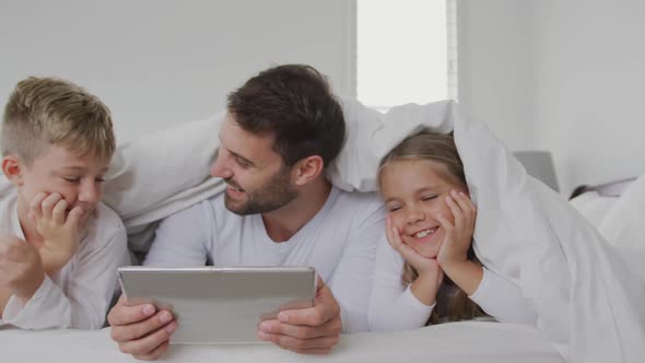 Father and children using digital tablet under blanket on bed at home 4k