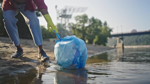 African American Man Catches Trash Bag with Plastic on Water