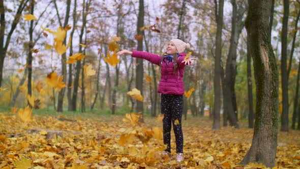 Joyful Girl Tossing Autumn Foliage Up Outdoors