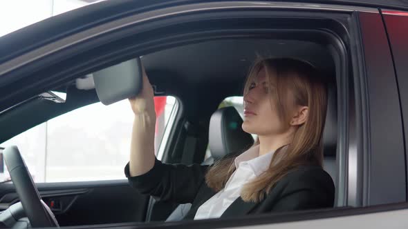 Beautiful Woman Looks in the Mirror in the Car at a Car Dealership