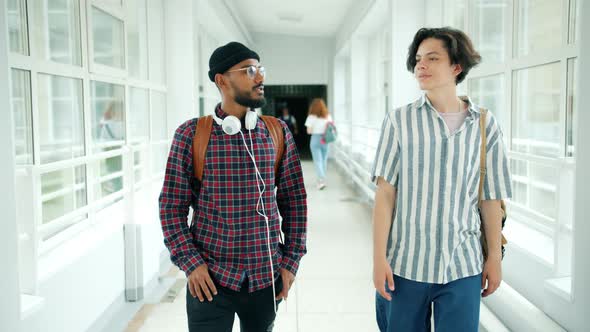 Male Students Walking in University Hall with Backpacks Talking After Classes