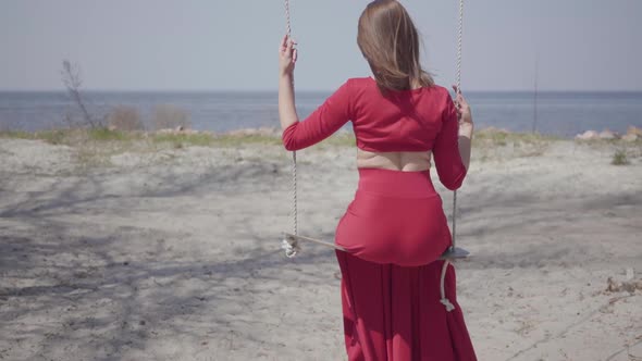 Portrait Slim Elegant Woman in Red Dress Sitting on the Swing and Looking an Amazing Spectacular