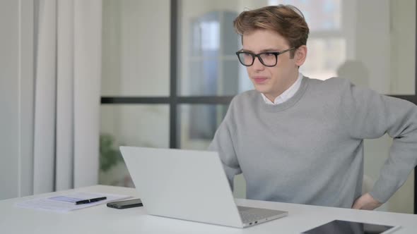 Young Man Having Back Pain While Using Laptop in Modern Office