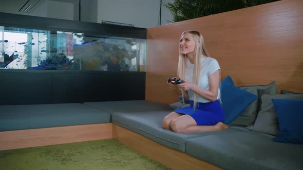 Woman Gaming and Relaxing in Modern Office. Young Formal Woman in Skirt Chilling on Sofa in