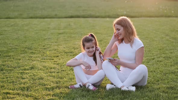 Mother and Daughter Are Listening To the Music on the Grass