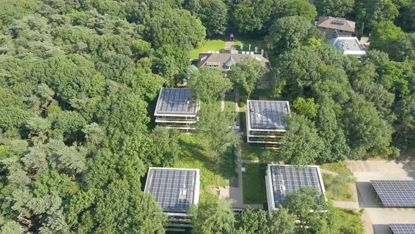 Aerial of small office buildings with solar panels on rooftop in a green forest
