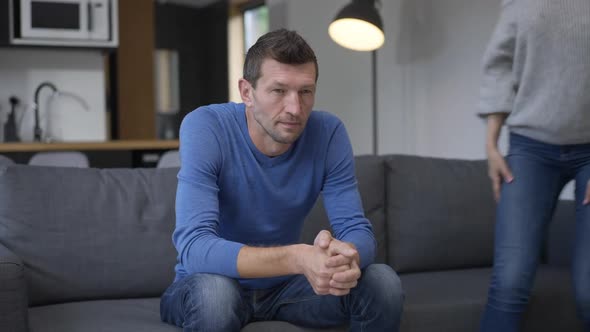 Adult Caucasian Man Sitting on Couch As Cheerful Woman Entering