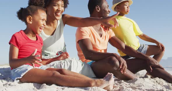 Smiling african american family sitting and embracing on sunny beach