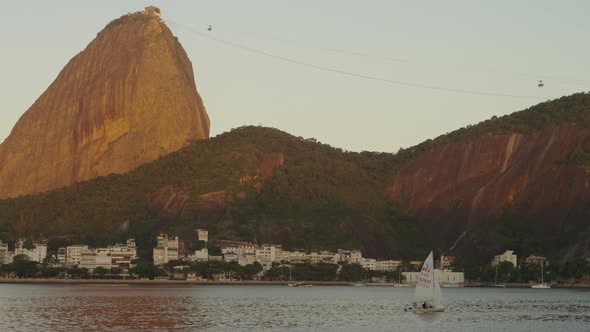 Static shot of a sailboat on Guanabara Bay with Sugarloaf Mountain in the distance.