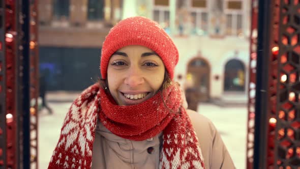 Happy Smiling Cheerful Young Woman in Knitted Red Cap and Scarf Walking on City Square with Festive