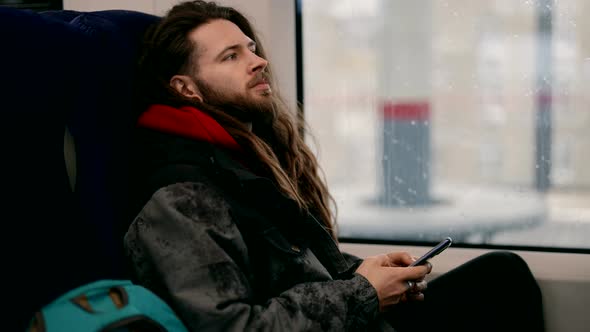 A Man with a Beard and Long Hair Who Uses a Smartphone on a Subway Train