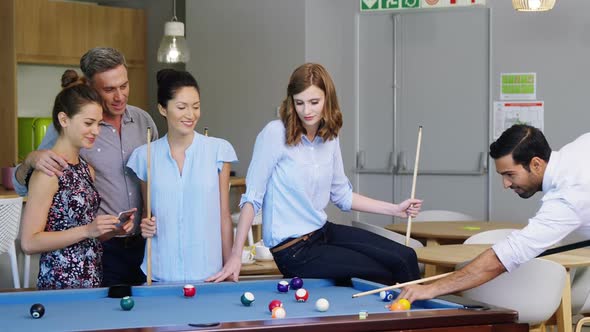 Executive taking picture with mobile phone while colleagues playing pool