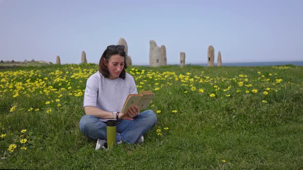 A Girl Reads a Book Sitting on the Green Grass