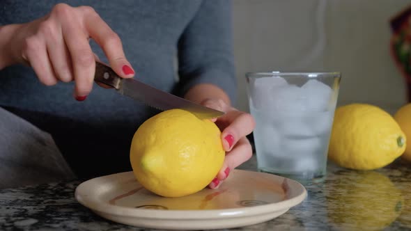 Woman cutting a lemon in half with a knife and glass of lemonade on the side