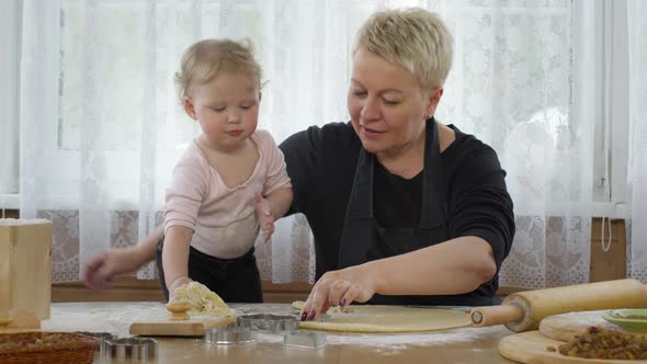 Little Cute Granddaughter Helps Granny Cook Dough for Pastry and Smiles.