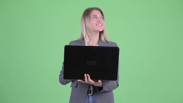 Happy Young Blonde Businesswoman Thinking While Using Laptop