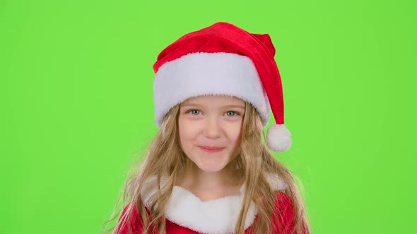 Child Girl in a Beautiful Suit and a Red New Year's Cap Smiles. Green Screen