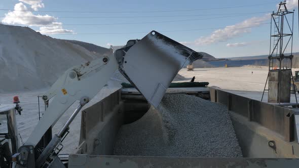 Bucket of Front Loader Loads Crushed Stone at Dump Truck Body at Construction Logistics Hub 