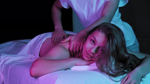 Massage Session in Neon Lighting Young Woman Lying on a Couch and Receiving a Massage and Looking in