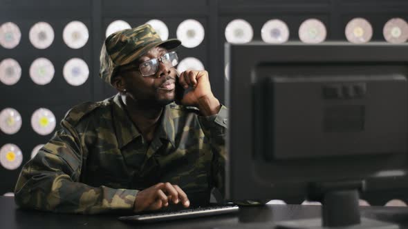 Handsome Black Male in Military Clothes Speaks on Phone and Looks at PC Display