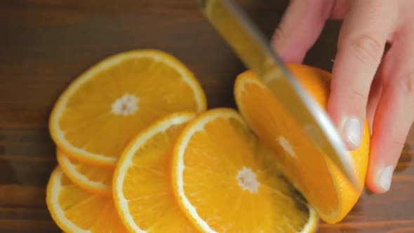 Male hand with big knife slicing orange citrus fruit on the cutting board at kitchen