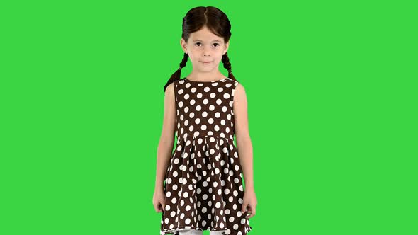 Little Girl in Polka Dot Dress Standing and Putting Hands To Her Head on a Green Screen Chroma Key