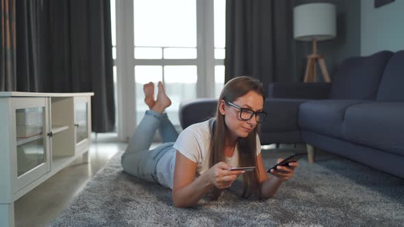 Woman Is Lying on the Floor and Makes an Online Purchase Using a Credit Card and Smartphone. Online