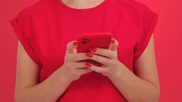 Unrecognizable Woman Writes Text Messages on Her Smartphone on a Red Studio Background