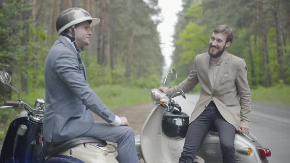 Two Confident Positive Caucasian Men Sitting on Retro Scooters on Countryside and Talking. Portrait