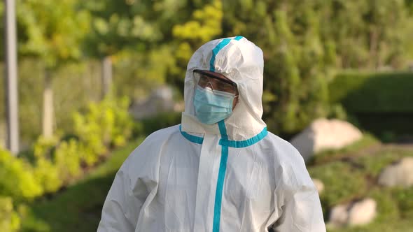 Portrait of a Young Man in a Protective Suit, Glasses and a Mask Looks at the Camera and Shows the