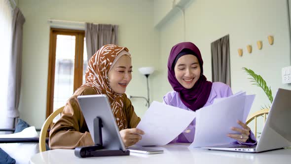 Two muslim women wearing hijab working together with using laptop tablet and paper showing chart 