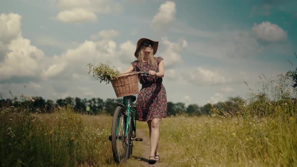 Tourist Girl Relaxing On Countryside Wildflower Field. Woman Cyclist Walking With Bike On Holiday.