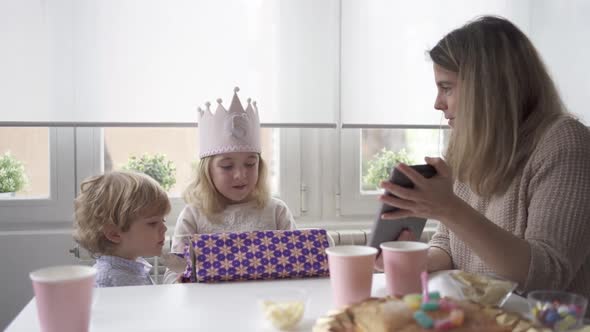 Amazed happy little girl unwrapping birthday present party at home