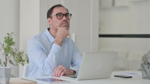 Middle Aged Man Thinking While Using Laptop in Office