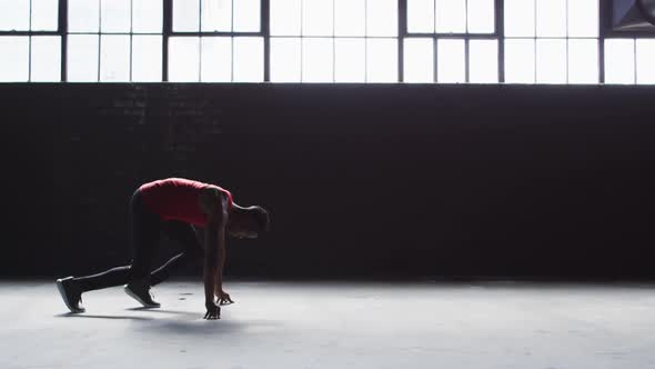 African american man kneeling starting a run in an empty building