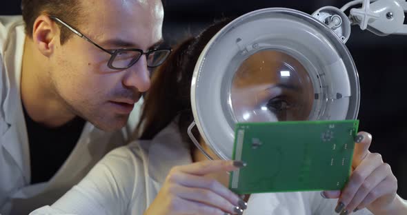 Couple of Technicians Studying Circuit Board with Magnifier