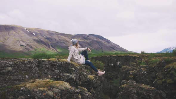 Happy Young Hipster Woman Sits on Rock with Mountains Background and Enjoying Nature Slow Motion