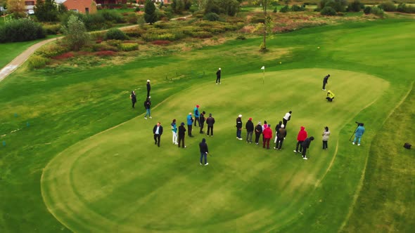 Aerial View of a Bunch of People Standing and Watching a Quick Game of Golf in a Small