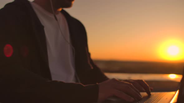 Vault Plan of a Hand Typing on a Laptop Keyboard at Sunset with a View of the City From a Height