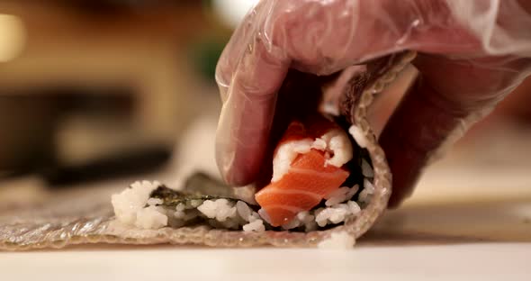 Hands Of A Sushi Chef Rolling Salmon Sushi Rolls By A Bamboo Mat In The Kitchen. Making Sushi Rolls.