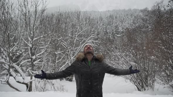 Content man in outerwear outstretching arms in winter forest