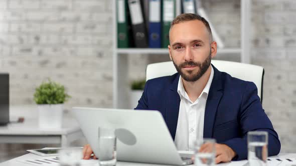 Portrait of Smiling Bearded Businessman in Suit Posing at Modern Light Office in Front of Laptop Pc