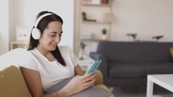 Happy Positive Young Adult Woman Using Phone While Listening to Music at Home