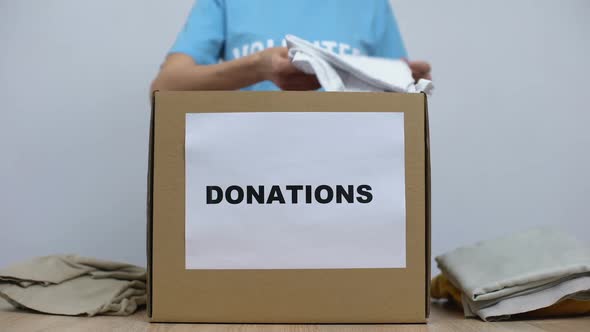 Kind Female Activist Putting Clothes in Donation Box on Table